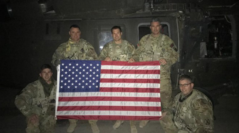 Soldiers from G Company 2-238th General Support Aviation Battalion, as part of Task Force Dragon while deployed to Afghanistan, pose for a photo during a mission with a flag flown to be sent home to their family members, Feb. 6, 2020. The training was done to comply with Army aviation regulations regarding rated and non-rated crewmember requirements. (U.S. Army National Guard courtesy photo)